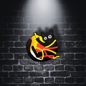 Puede incluir: Parche bordado de un gato negro con hilo amarillo y naranja envuelto a su alrededor. El gato mira hacia la derecha con una expresión de sorpresa.