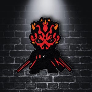 May include: A red and black embroidered patch of Darth Maul from Star Wars. The patch features a cartoon-style depiction of Darth Maul with his signature double-bladed lightsaber.