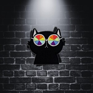 Peut inclure: Patch brodé noir de chat avec des lunettes de soleil arc-en-ciel. Le patch est sur un fond de brique foncé.
