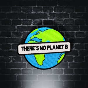 Puede incluir: Un parche bordado azul y verde de la Tierra con una pancarta blanca en el medio que dice "THERE'S NO PLANET B".