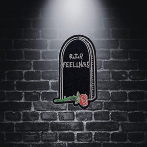 Puede incluir: Parche bordado negro con un diseño de lápida. La lápida tiene las palabras "R.I.P. FEELINGS" en ella. Una rosa roja con hojas verdes se encuentra en la base de la lápida.