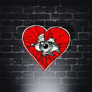 May include: A red heart-shaped patch with a white eye in the center. The heart is cracked and broken into many pieces.