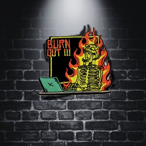 May include: An embroidered patch depicting a skeleton sitting at a laptop with flames surrounding it. The text "BURN OUT III" is on a black background behind the skeleton.