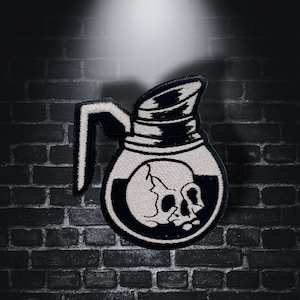 Peut inclure: Patch brodé noir et blanc d'une cafetière avec un crâne à l'intérieur. La cafetière a une poignée et un bec verseur. Le crâne est détaillé avec des orbites et un nez.