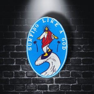 May include: A blue and white embroidered patch with the text "Surfing Like A God" and a cartoon image of a person surfing on a wave.