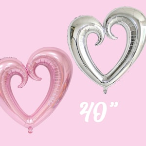 May include: Two large heart-shaped foil balloons, one pink and one silver, with a curled design. The balloons are 40 inches in size.