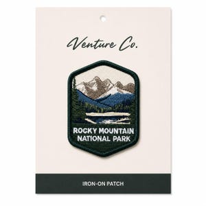 Könnte beinhalten: Ein Aufbügler mit einer Berglandschaft mit See und Bäumen. Der Aufnäher hat einen dunkelgrünen Rand und den Text "Rocky Mountain National Park". Der Markenname "Venture Co." steht oben.