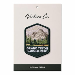 Könnte beinhalten: Ein aufbügelbarer Aufnäher mit einer Berglandschaft und dem Text "Grand Teton National Park". Der Aufnäher ist grün und schwarz, mit "Venture Co." in Schreibschrift oben. Der untere Teil der Karte lautet "Iron-on Patch".