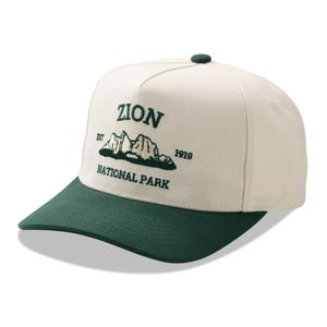 May include: A cream-colored baseball cap with a dark green bill and button. The cap features the text "ZION NATIONAL PARK" in dark green, along with an embroidered mountain graphic. The year "1919" is also displayed.