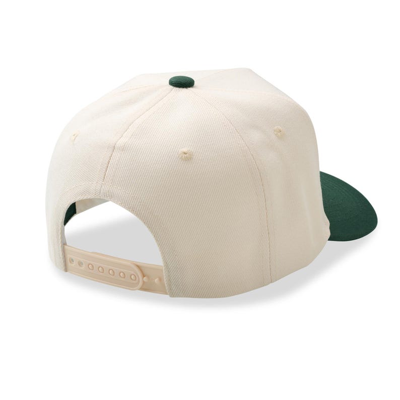 May include: Cream-colored baseball cap with a dark green brim and button. The cap has a snapback closure and a structured design. The back of the cap is visible, showing the adjustable strap.