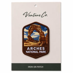 Pode incluir: Um patch de passar a ferro com o icónico Delicate Arch do Parque Nacional Arches. O patch tem uma borda castanha e uma imagem bordada detalhada do arco sob um céu azul. O texto "ARCHES NATIONAL PARK" é exibido abaixo.