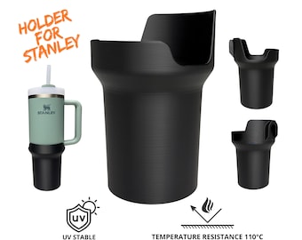 Può includere: Porta bicchiere in plastica nera per un bicchiere da viaggio Stanley con cannuccia. Il porta bicchiere è progettato per mantenere il bicchiere in posizione verticale e sicura. Il testo "HOLDER FOR STANLEY" è scritto in arancione su sfondo bianco. Il porta bicchiere è stabile ai raggi UV e resistente a temperature fino a 110 gradi Celsius.