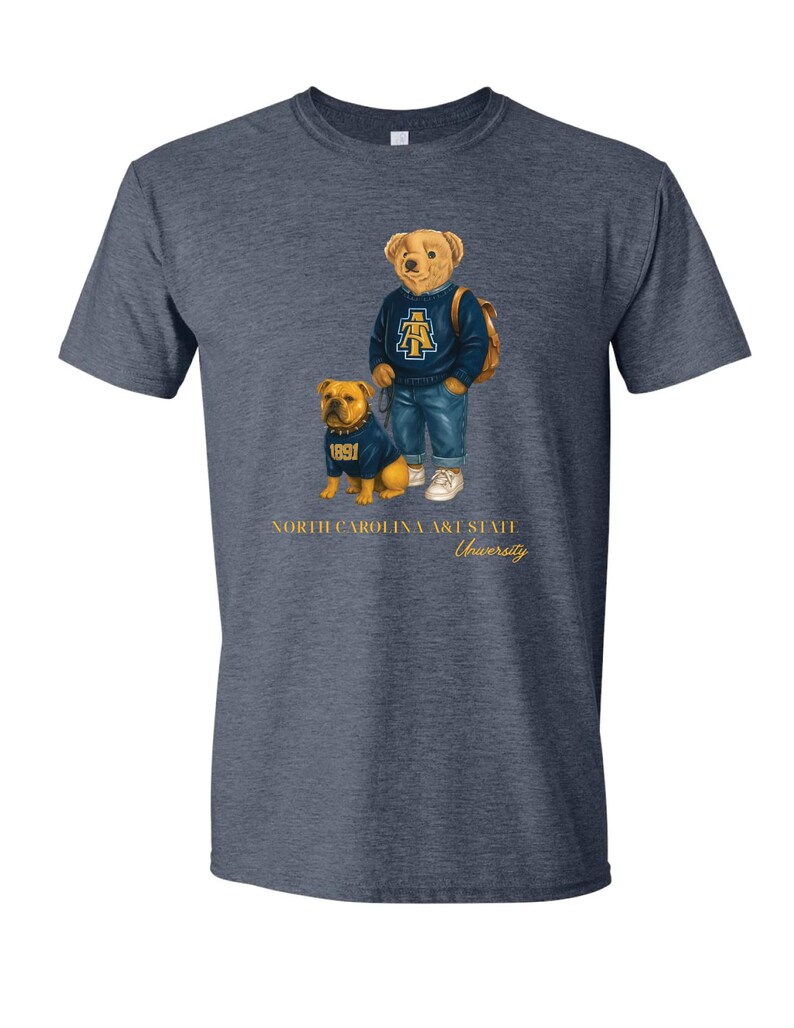 以下が含まれることがあります： ネイビーブルーのTシャツ。クマと犬のイラストが描かれています。クマは青いセーターとジーンズを着ており、犬も同じセーターを着ています。「NORTH CAROLINA A&T STATE University」の文字が下に印刷されています。