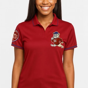 May include: A red polo shirt with blue trim and a collared neckline. The shirt features a bulldog mascot patch with the letters "SC" and a university logo on the sleeve. The shirt is made of a lightweight material.