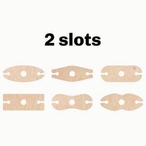 May include: Six different wooden wine bottle holders, each with two slots. The holders are in various shapes, including oval, rectangular, and a figure eight. The text "2 slots" is printed above the holders.
