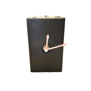 Puede incluir: Una cámara vintage negra convertida en un reloj con manecillas rosas. La esfera del reloj está en la parte delantera de la cámara.