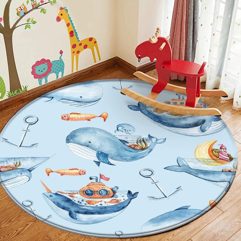 May include: A round blue rug with a nautical theme featuring whales, anchors, and a submarine. The rug has a light blue background with white outlines around the images.