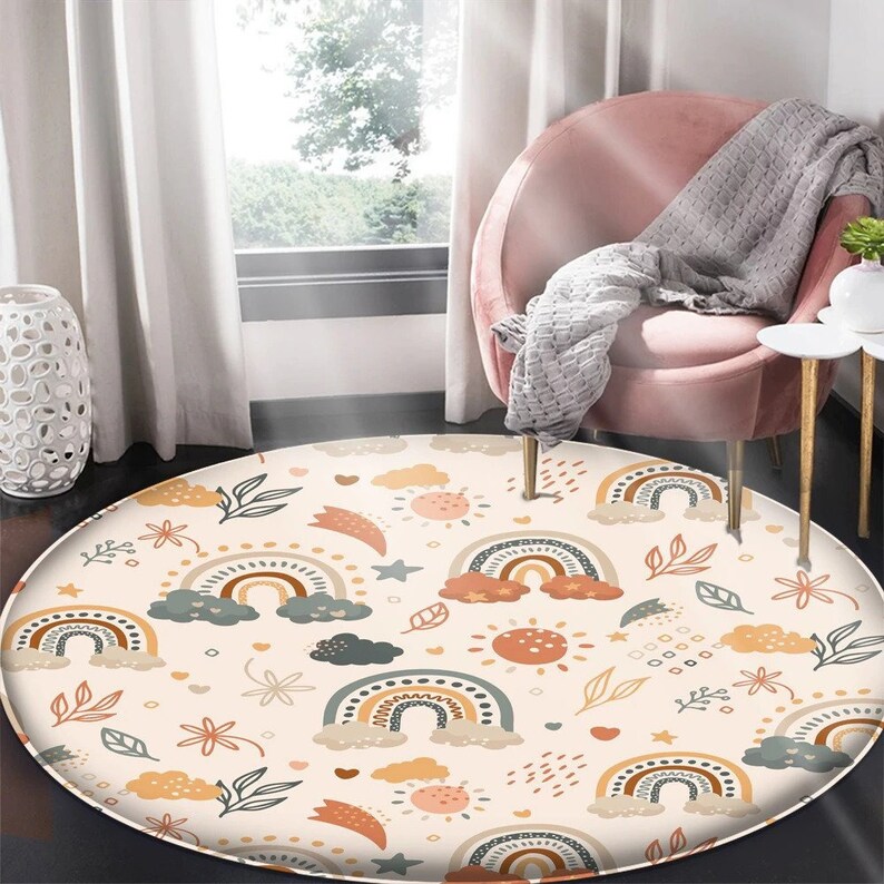 May include: A round cream-colored rug with a repeating pattern of rainbows, clouds, stars, and suns in shades of orange, yellow, brown, and green. The rug is on a light wood floor.
