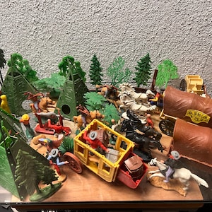 Può includere: Un set di giocattoli vintage con cowboy, nativi americani, cavalli, carri e tepee. Il set è in plastica ed è in buone condizioni. I giocattoli sono dipinti in vari colori, tra cui marrone, verde, rosso e giallo.