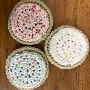 May include: Three crocheted coasters with a brown outer edge and a white or pink center with colorful sprinkles.