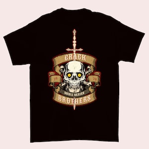 Op de afbeelding: Zwart t-shirt met een schedelafbeelding met gele ogen, gekruiste botten en een zwaard. Het ontwerp bevat de tekst "CRACK SKULL SERIES BROTHERS" en de nummers "20" en "23" op een banner.