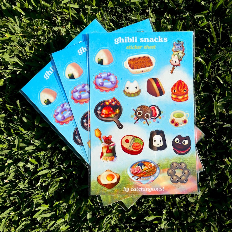 Puede incluir: Varias hojas de pegatinas azules con ilustraciones coloridas de snacks Ghibli. Cada hoja presenta varios alimentos como donuts, onigiri y postres. El texto "Ghibli snacks sticker sheet" est&aacute; impreso en la parte superior de la hoja, con el nombre del artista en la parte inferior.