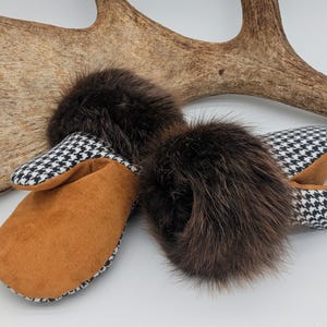 May include: A pair of brown and tan mittens with a black and white houndstooth pattern. The mittens have a brown fur accent on top and are set against a light background with a large antler.