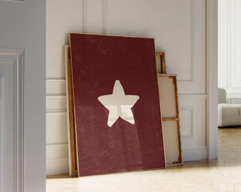 May include: A framed canvas print with a white star on a burgundy background. The canvas is leaning against a white wall.