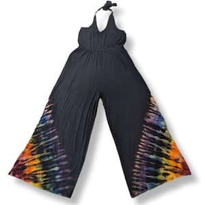 May include: Black halter-neck jumpsuit with wide legs. The lower sides of the legs feature a vibrant tie-dye pattern in shades of red, orange, yellow, blue, and purple. The jumpsuit has a gathered waist and a halter tie.