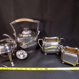May include: A silver tea set with a teapot, creamer, sugar bowl, and a stand. The set has a polished finish and intricate details.
