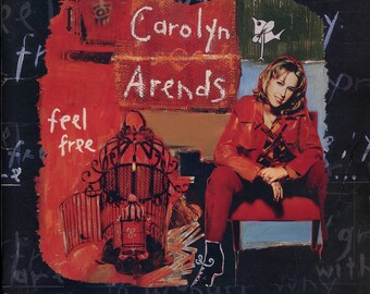 May include: A red and white album cover with a woman in a red jacket sitting on a red chair. The album cover is titled "Feel Free" and features the artist's name, "Carolyn Arends".