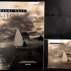May include: A CD and sheet music for the album "Le Voyage" by Sandi Patti. The cover art features a sailboat on a lake with mountains in the background. The text "Medium Voice Range" is printed on the sheet music.