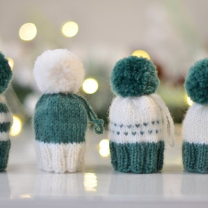 May include: Four knitted hats with pom-poms in white and green. The hats have different patterns, including stripes and hearts.