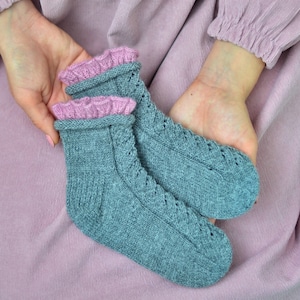 Può includere: Un paio di calzini di lana grigi con bordino in pizzo rosa. I calzini sono tenuti nelle mani di una persona che indossa un vestito rosa.