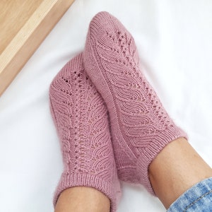 Könnte beinhalten: Ein Paar rosa gestrickte Socken mit einem Spitzenmuster. Die Socken sind knöchellang und haben ein zartes, feminines Design.