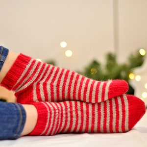May include: A pair of red and white striped socks with a fuzzy texture. The socks are folded over each other and are lying on a white surface.