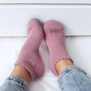 Könnte beinhalten: Ein Paar rosa gestrickte Socken mit gerippter Struktur. Die Socken werden an den Füßen einer Person getragen und die Knöchel sind sichtbar.