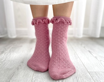 May include: A pair of pink knitted socks with a ruffled trim at the top. The socks have a delicate, lacy pattern.