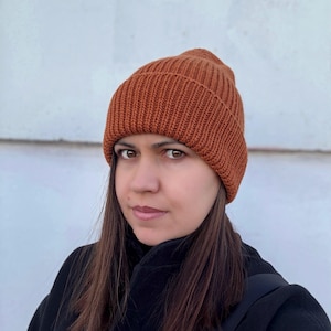 Puede incluir: Primer plano de una persona que lleva una boina de punto marrón. La boina está hecha de un hilo suave y texturizado y tiene un diseño simple y clásico.