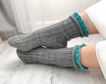 May include: A pair of gray knitted socks with teal ruffled trim. The socks are folded over each other and the teal trim is visible on both socks.