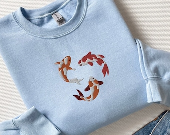 May include: A light blue sweatshirt with a design of three orange and white koi fish swimming in a circle.