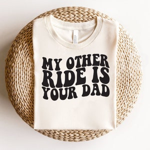 May include: A white t-shirt with black text that reads "My other ride is your dad" in a retro font.