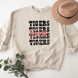 May include: A beige sweatshirt with the word "TIGERS" repeated four times in black with a red "TIGERS" in the middle.