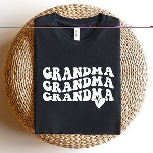 May include: Black t-shirt with white text that reads "Grandma Grandma Grandma" with a small white heart.