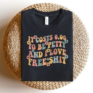 May include: Black t-shirt with a retro-style graphic that says "It costs 0.00 to be petty and I love free shit" with colorful flowers surrounding the text.