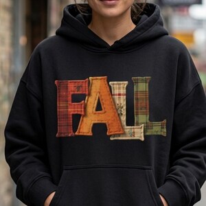 May include: A black hooded sweatshirt featuring the word FALL across the chest. Each letter is rendered in a different fabric pattern: the F is red plaid, the A is solid orange, the L is cream plaid, and the second L is green plaid.