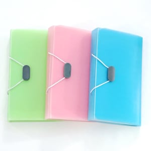 May include: Three colorful document folders in green, pink, and blue. Each folder has a matching elastic band closure with a gray clasp. The folders are arranged side by side against a white background.