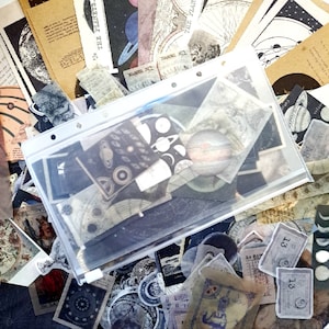 May include: A clear plastic bag filled with various vintage paper ephemera, including illustrations of planets, stars, and celestial bodies. The ephemera is printed on brown, white, and black paper. The bag is open and the ephemera is spilling out.
