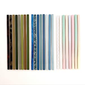May include: A collection of 30 decorative washi tape strips in various colors and patterns. The strips are arranged in three rows of ten. The first row features brown, green, and beige strips. The second row features blue and teal strips. The third row features pink, white, and light blue strips.