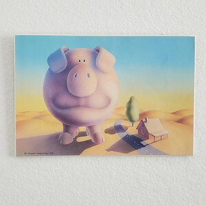 May include: A rectangular art print featuring a large, round, light pink pig standing in a desert landscape. A small house and a single tree are situated near a winding road in the background under a clear blue and yellow gradient sky.